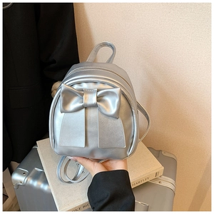 Silver bow-knot backpack in metallic finish placed on a suitcase for travel style
