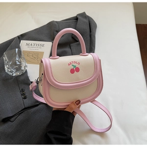 Detail of color-block pink and cream handbag with cherry print on a flat lay background