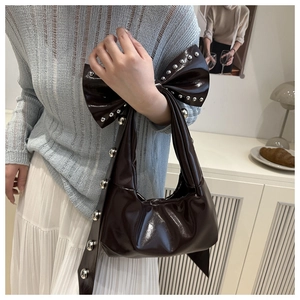 Detail of dark red patent leather shoulder bag with bow and silver studs on a cloud-like base