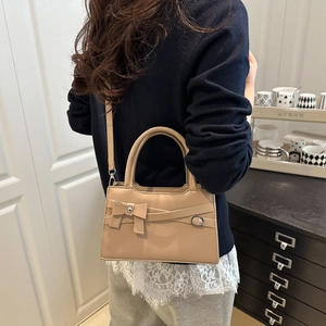 Elegant beige crossbody handbag with bow detail and round handle shown in lifestyle setting