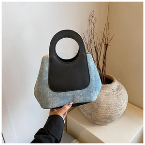 Detailed view of light blue denim and black leather tote bag with rhinestone embellishments