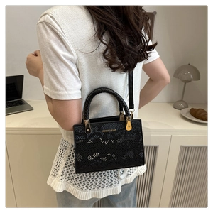 Detail of black snake pattern shoulder bag featuring golden metal hardware and woven handle