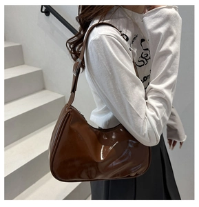Close-up of a brown glossy hobo bag with adjustable silver buckle strap on a model
