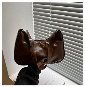 Close-up of brown glossy leather hobo bag with adjustable strap and silver metal buckle