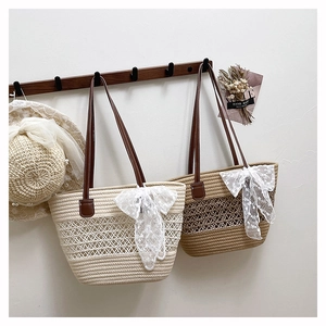 Détail d'un sac cabas en paille tissée avec nœud en dentelle et poignées en cuir sur support