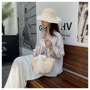 Detail of handmade woven straw bucket bag and pearl hat with lace bow on a street bench