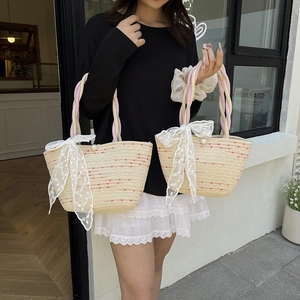 Handwoven straw tote bag with pink rope handles and large white lace bow detail