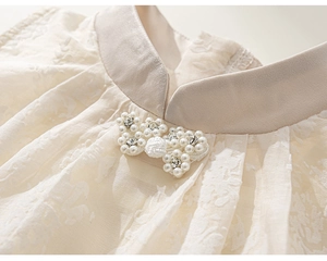 Détail du col montant avec nœud en perles et texture dentelle sur une robe crème