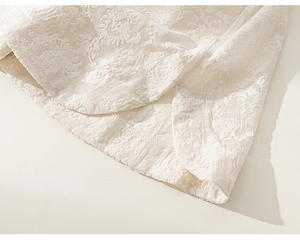 Détail du tissu jacquard floral et de l'ourlet fendu de la robe chinoise blanc ivoire
