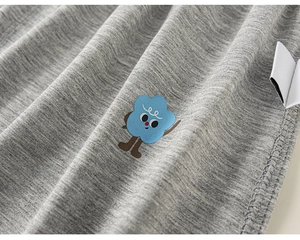 Detailed close-up of grey cotton knit fabric with a small blue cloud cartoon print and side label