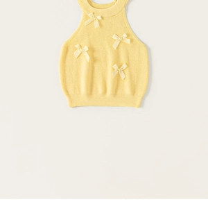 Close-up of light yellow knit vest featuring sweet ribbon bows and ribbed texture