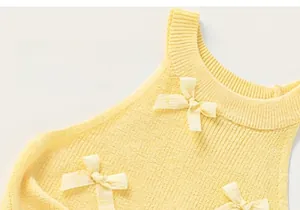Detail view of yellow knitted cotton toddler vest with decorative white bow accents