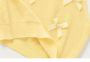 Close-up of pale yellow knit fabric with 3D texture and delicate cream bow details