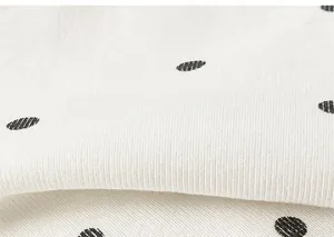 Gros plan sur un tissu tricoté blanc à pois noirs montrant la texture douce et le tissage