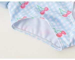 Détail de maillot de bain bébé avec motif vichy bleu clair et imprimé cerises roses
