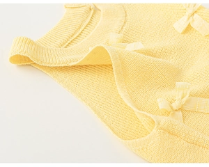 Detail of light yellow knit top featuring a ribbed neckline and cute bow embellishment