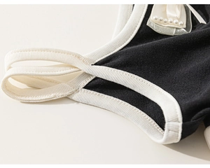 Detail of knit dress featuring contrast trim, elegant satin bow and white pearl accents