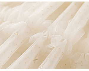 Detail of off-white mesh fabric with sparkling gold sequins and layered pleats on girl dress