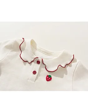 Detail of baby girl short sleeve top featuring strawberry embroidery and wavy red trim
