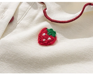 Detail of red strawberry embroidery on cream cotton T-shirt with wavy red trim and button