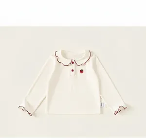 Detail of girl's cream long-sleeve top featuring red scalloped trim and strawberry embroidery