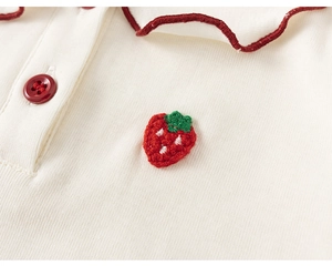 Detail of knit shirt showing a red resin button and handmade crochet strawberry patch