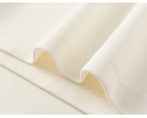 Detailed close-up of cream knit cotton fabric with professional ribbed hem stitching