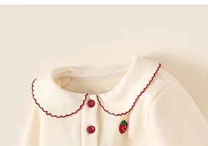 Detail of baby girl cream top with Peter Pan collar, strawberry embroidery and red buttons