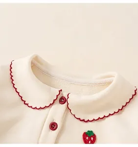 Detail of Peter Pan collar with red embroidery and strawberry patch on cream kids top