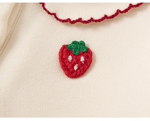 Close-up of strawberry embroidery and red ruffled collar on a cream cotton shirt