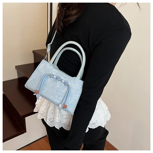 Detail of light blue jacquard bucket bag with floral texture and pearl beaded tassel charm