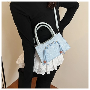 Detail of light blue crossbody bag with unique pebbled texture and woven knot charm