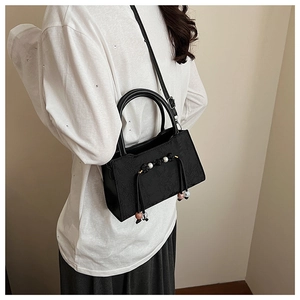 Detail of black embossed crossbody bag with pearl tassels worn by a model in soft light