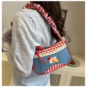 Detail of denim shoulder bag with red gingham strap and cherry embroidery accent