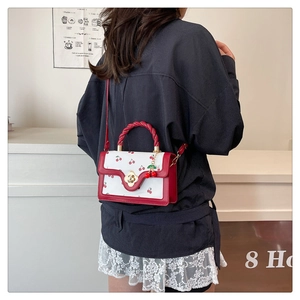 Detail of red and white cherry print handbag with golden floral clasp and cherry charms