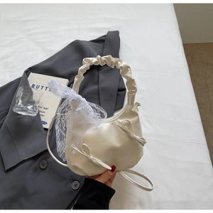 Détail d'un sac à main plissé blanc crème avec nœuds en cuir et écharpe en dentelle décorative