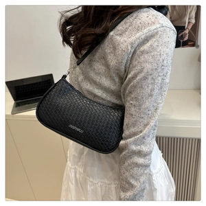 Detailed close-up of a black woven shoulder bag with white lettering and metal zipper