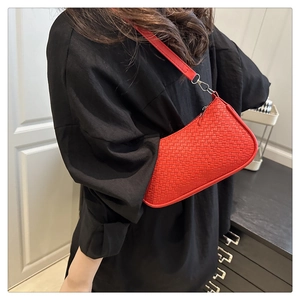 Detail of red woven texture shoulder bag with top zipper and matching strap worn by a model