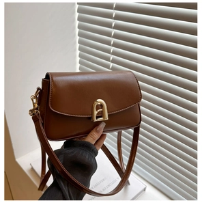 Detail view of a luxury brown leather crossbody bag with a distinctive gold arc metal clasp