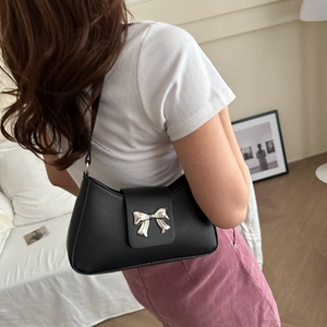 Chic black leather underarm bag with a silver metal bow accent in a minimalist setting