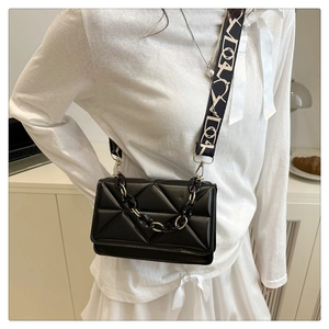 Detail of black quilted crossbody bag with resin chain and patterned fabric strap