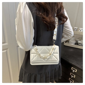 Detail of white quilted handbag featuring triangular stitching and branded wide strap