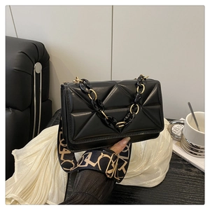 Detail of black quilted shoulder bag with gold chain and patterned jacquard strap