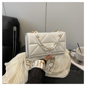 Detail of white quilted crossbody bag showing acrylic chain and wide canvas shoulder strap