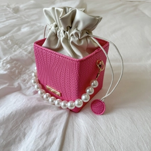 Detail of pink woven bucket bag featuring pearl handle and cream drawstring liner