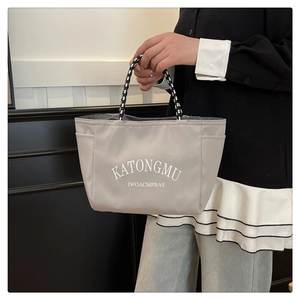 Detail view of the gray minimalist tote bag with braided handles and letter print