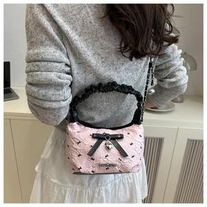 Detail of pink pleated handbag with black bows and heart pendant shown on model