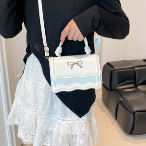 White mini crossbody bag with wavy flap, gold bow, and woven handle for women