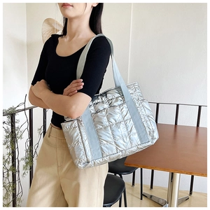 Silberne Stepp-Tragetasche mit Metallic-Finish und breitem Schultergurt an einem Model