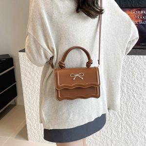 Brown faux leather crossbody bag featuring a golden ribbon bow and wavy edge design